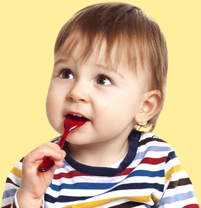 A toddler in a striped shirt chews on a red spoon in front of a yellow background.