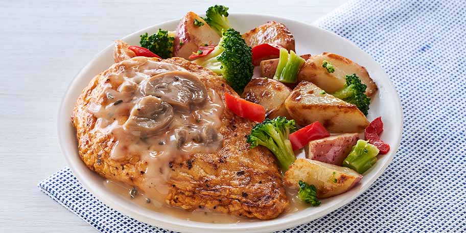 A plate of herb roasted chicken with potatoes, broccoli and mushrooms on a cloth napkin.
