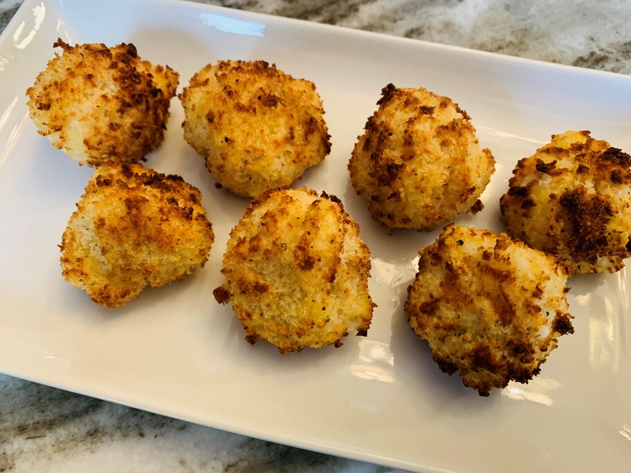 Seven mac and cheese bites on a white plate on a kitchen counter.