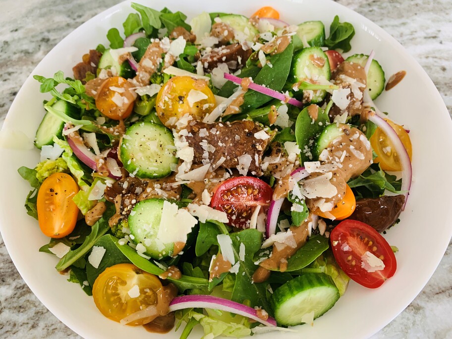 A white plate full of salad with cucumbers, tomatoes, onions, cheese and steak portabella.