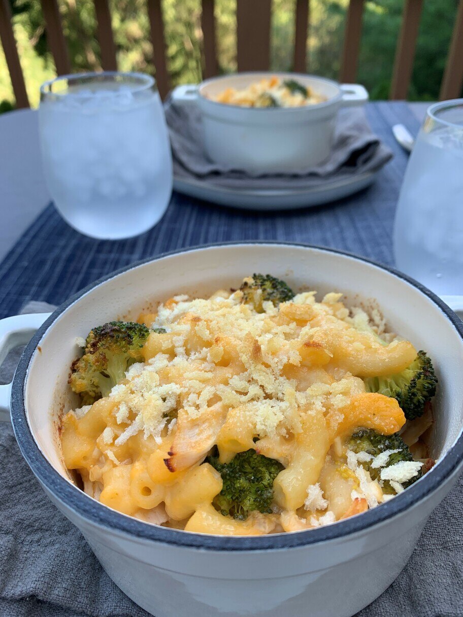 A patio table set with glasses of water, napkins and two casserole dishes of baked mac and cheese with broccoli.