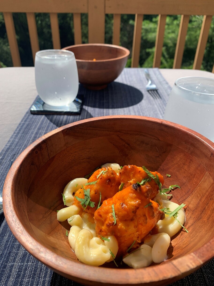 A patio table set with glasses of water, tablecloth, napkins and two wooden bowls of mac and cheese with buffalo chicken.