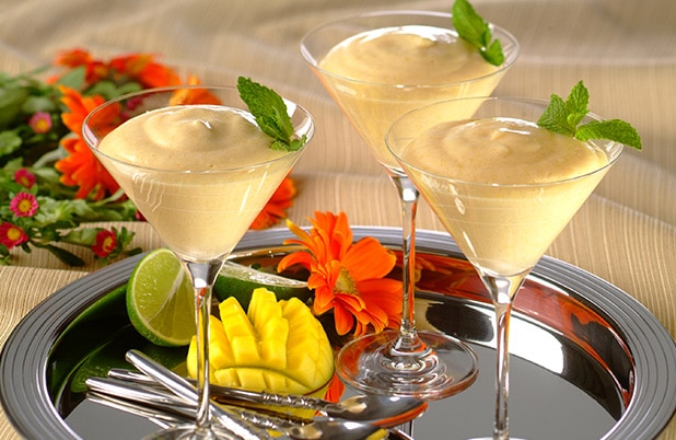 Copas de Martini llenas de mousse de mango sobre una bandeja de plata con un mango y cucharas.