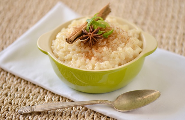 Un plato color verde lleno de arroz con leche estilo cubano cubierto con cáscara de limón agrio, anís y ramitas de canela.