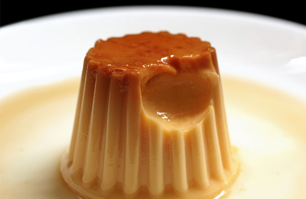 Un pequeño flan en un plato blanco al que le falta un bocado.