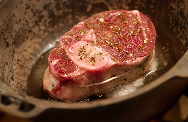 A piece of steak searing in a skillet with spices and herbs.