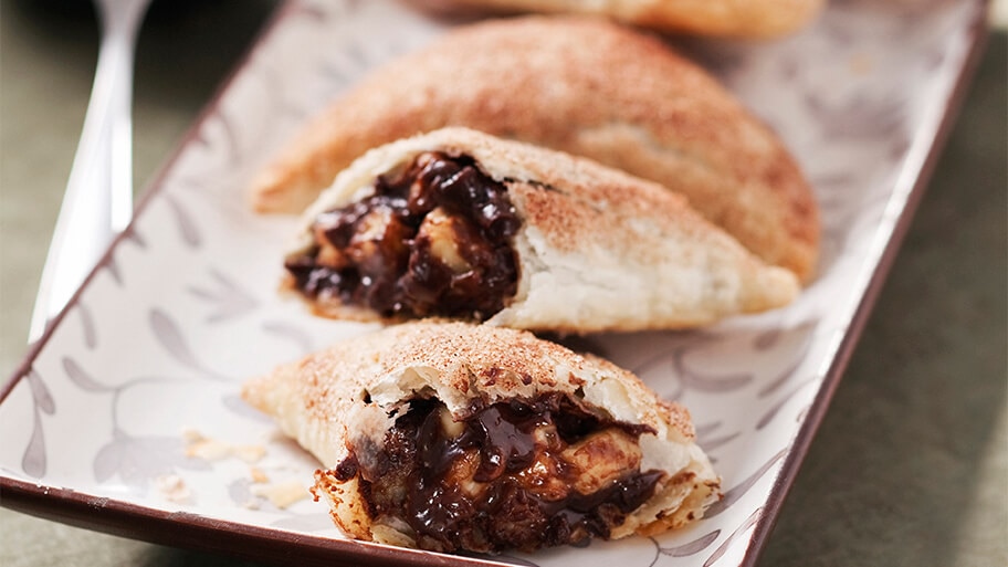  Empanada recién horneada de chocolate y banana cortada a la mitad mostrando el relleno sobre una bandeja de cerámica.