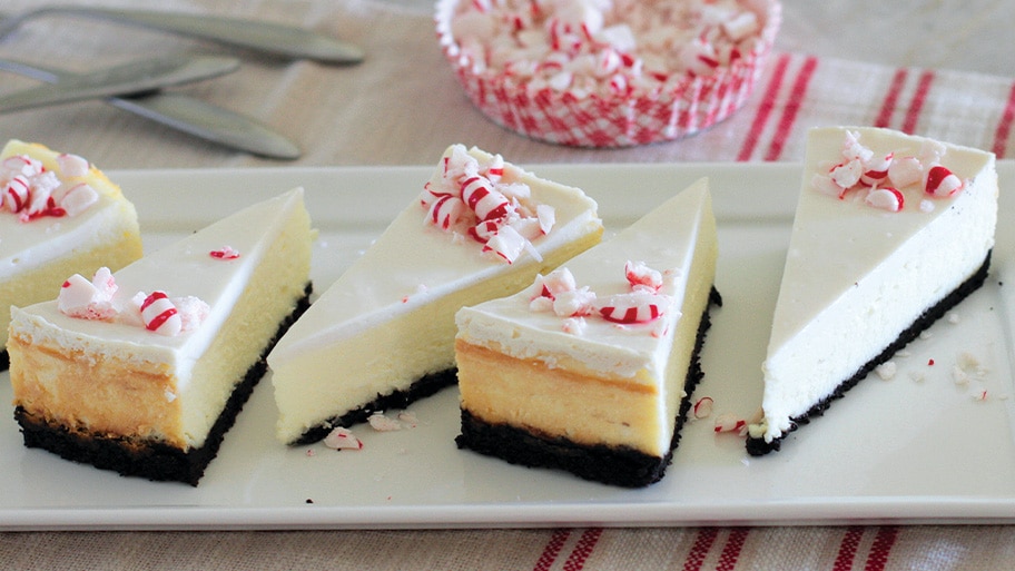 Five slices of Peppermint Mocha Cheesecake on a white plate by a dish of crushed peppermints on a red striped towel.