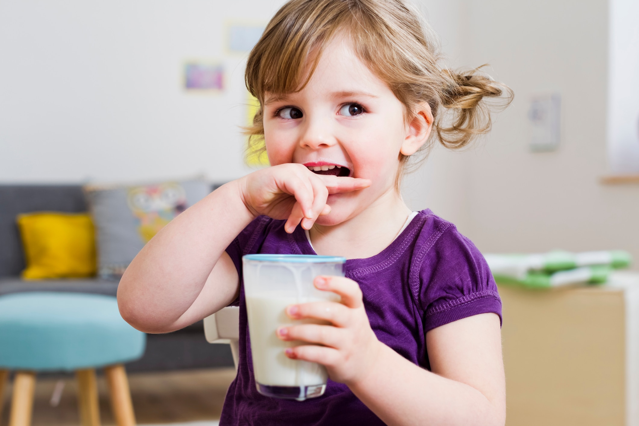 Una niña se muerde el dedo mientras sostiene una taza de NIDO.