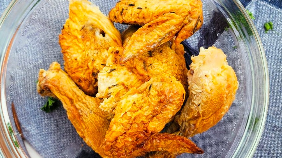 A bowl of leftover chicken on a cloth napkin with scattered herbs.