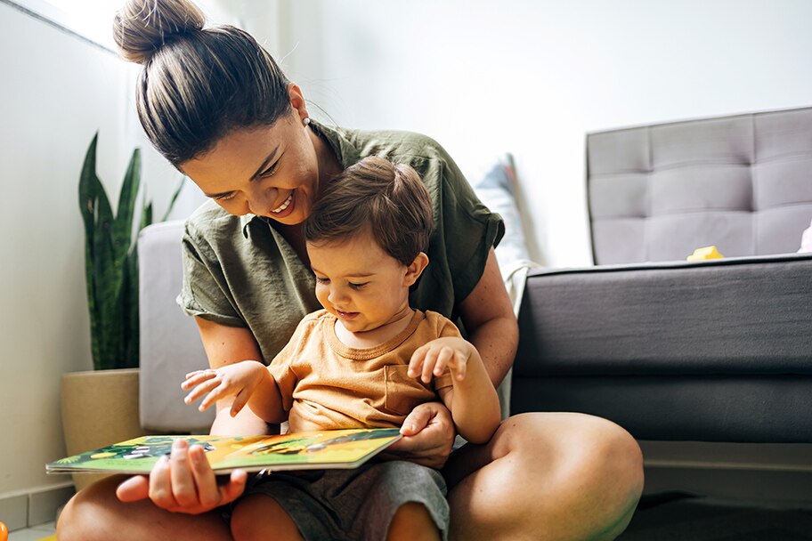 Una mujer lee un libro de cuentos a su niño pequeño en un dormitorio.