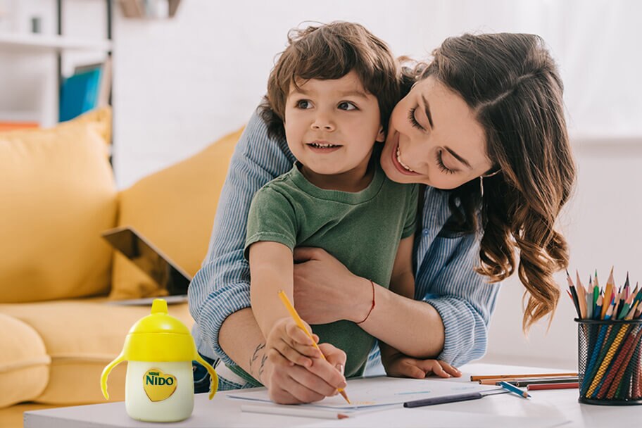 Mamá y pequeño dibujando en una sala de estar con una botella de NIDO sobre la mesa.