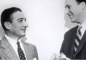 A black and white photo of men in suits talking.